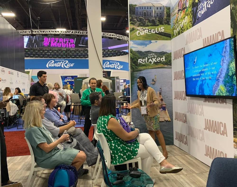 Chevonne Palmer, Director of Sales, Island Routes, supported by John Woolcock, Manager, Groups & Conventions, Jamaica Tourist Board (standing at center), presenting to enrapt meeting planners at Jamaica’s booth at IMEX.